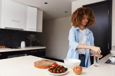 Mutfakta elinde meyve ve sebzelerle duran kıvırcık saçlı bir kadın. Sağlıklı yaşam tarzı kavramı.