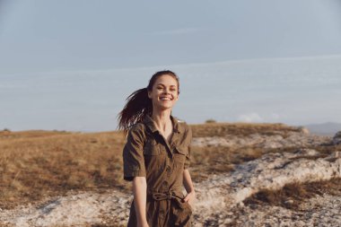 Yeşil tulumlu kadın kayalık tepede duruyor. Arka planda mavi gökyüzü var. Macera ve seyahat kavramı.