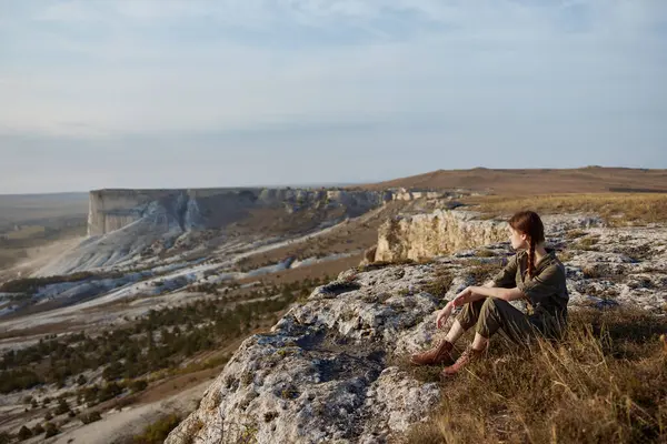 Stock image Woman sitting on edge of cliff admiring majestic valley and mountains landscape view, travel adventure nature beauty concept