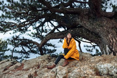 Zarif sarı ceketli sakin bir kadın görkemli bir dağ manzarasının önünde doğayı düşünür.