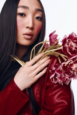 Uzun siyah saçlı, kırmızı ceketli şık bir kadın elinde güzel bir buket çiçek tutuyor.