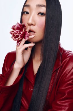 Uzun siyah saçlı, kırmızı deri ceketli, elinde narin bir çiçek tutan çekici bir kadın.