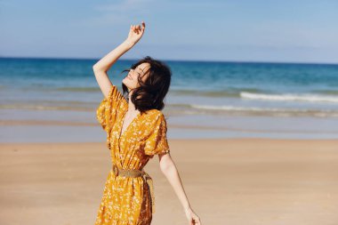 Okyanusun kıyısındaki kumlu sahilde kollarını açmış canlı sarı elbiseli bir kadın.