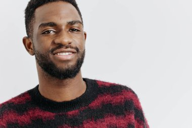 Kırmızı ve siyah süveterli, sakallı, kendine güveni tam, beyaz arka planda duran kendine güvenen, kendine güvenen genç bir adam..