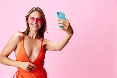 Canlı yaz titreşimleri turuncu mayo giymiş şık bir kadın pembe arka planda selfie çekiyor.