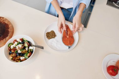 Kadın taze sebzelerle sağlıklı yemek pişiriyor ve mutfak tezgahında yağsız et yiyor.