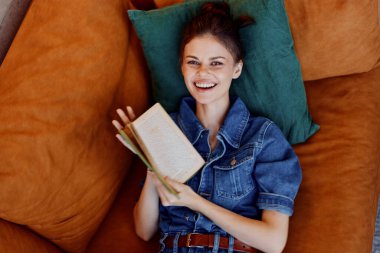 Elinde kitapla kanepede dinlenen ve huzur içinde gülümseyen mutlu bir kadın.