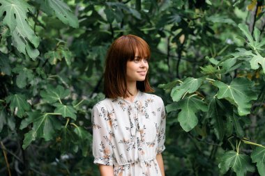 Çiçekli elbiseli kadın ormandaki yemyeşil çiçeklerle çevrili.