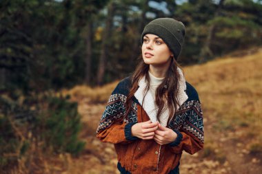 Şık şapkalı ve ceketli genç bir kadın sakin bir ormanda tepede dururken doğanın güzelliğinin tadını çıkarıyor.
