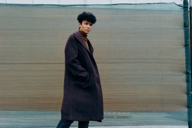 Moda: Mor ceketli kadın ve siyah / beyaz çizgili atkı elleri ceplerinde yeşil tel örgülerin önünde duruyor..