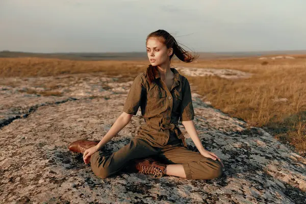 stock image Woman sitting on top of rock in grassy field, enjoying serene nature beauty and peaceful travel experience