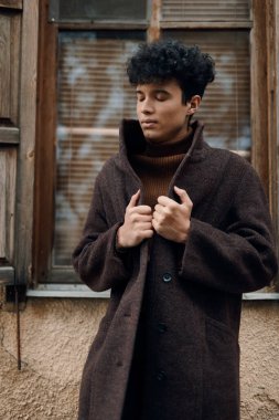 Moda genç adam kahverengi ceketli kaplumbağa yakalı kazak pencerede duran palto üzerinde eller.