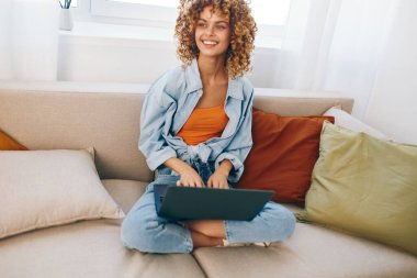 Konforlu Oturma Odasında Dizüstü bilgisayarda Çalışan Gülümseyen Kadın: Modern Ev Çalışmalarını Kucaklayan Güzel Bir Serbest Çalışmacı.