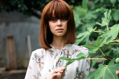 Canlı kızıl saçlı kadın yemyeşil yapraklara karşı poz veriyor.