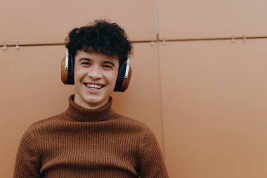 Turuncu bir duvarın önünde kulaklık takan gülümseyen bir gencin moda portresi. fotoğraf - resim fotoğrafçılığı.