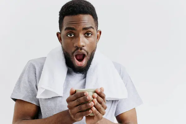 stock image A surprised young african american man holding a cup of coffee, isolated on a white background, reacting to unexpected news.