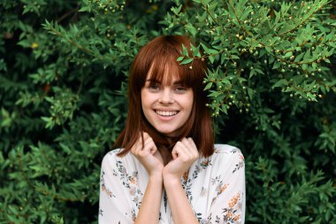 Canlı kızıl saçlı, yemyeşil yaprakların önünde zarif bir şekilde duruyor.