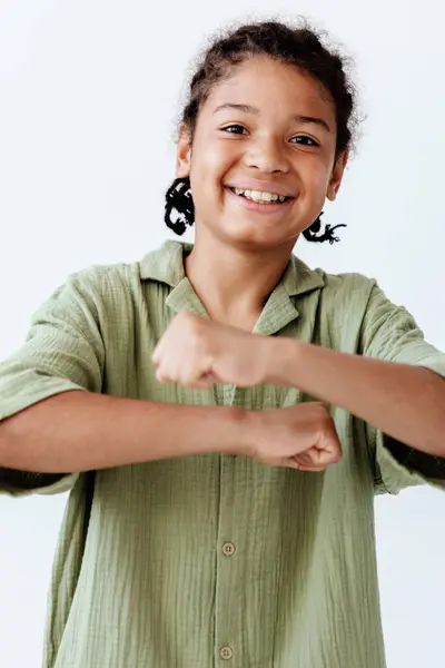 Stock image Young african american boy exudes confidence with raised fist, symbolizing strength and determination on a clean white background.