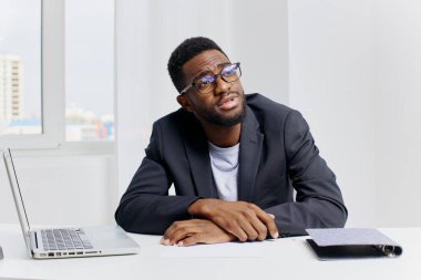 Takım elbiseli Afro-Amerikan iş adamı şık, modern bir ofis masasında dizüstü bilgisayarla yazı yazıyor..