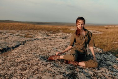 Huzurlu arazide bir kayanın üzerinde dinlenen, bacak bacak üstüne atan, seyahat macerası konsepti