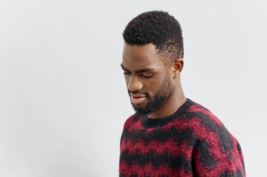 Şık, kırmızı ve siyah süveterli, kendine güvenen, modern moda ve özgüven dolu genç bir adam sade bir arka plana karşı ayakta duruyor..