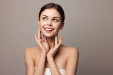 Gri bir arkaplan önünde kameraya bakan elleri yüzünde olan çekici genç bir kadın. moda ve güzellik konsepti.