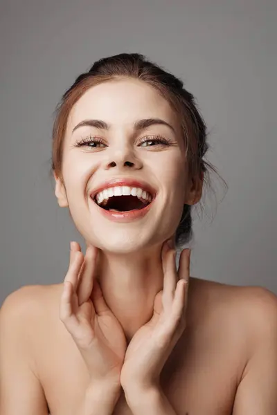 stock image Young woman smiling with hands on face, on gray background. royalty-free image.