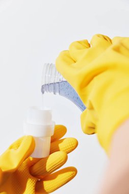 Sarı eldivenli bir kadın, şişeden başka bir kadının eline el dezenfektanı döküyor. Hijyen ve mikroplara karşı koruma kavramı.
