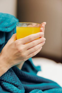 Mavi battaniyeye sarılmış bir adam elinde bardak ve bir fincan portakal suyu tutuyor..