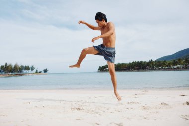 Kum üzerinde Koşan Asyalı Kaslı Sporcu: Sahilde Gün Batımında Özgürlük ve Gücün Portresi