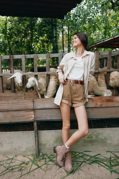 stock image A woman standing in front of a fence with sheep in a pen next to her