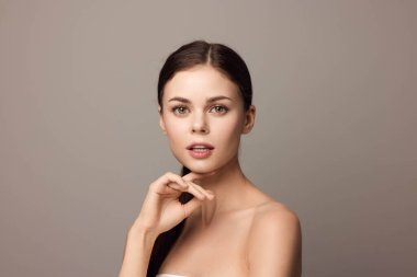 Çenesinde elleri olan genç bir kadın, kameraya bakıyor. Gri arka planda yakın plan portresi. güzel ve kendinden emin.