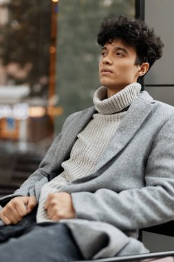 Gri bir kazak, siyah ceket, beyaz balıkçı yaka ve siyah pantolon giyen genç bir adamın moda fotoğrafı..