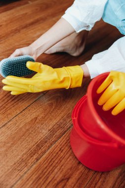 Ahşap zemini paspas ve plastik eldiven takan bir kova suyla temizleyen kadın..
