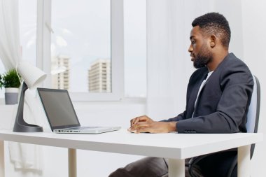 Uzaktan kumandalı takım elbiseli bir profesyonel modern, aydınlık bir odadaki bir masada dizüstü bilgisayar kullanıyor..