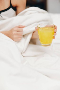Yatakta beyaz çarşaflı bir adam, elinde bir fincan portakal suyu tutuyor..