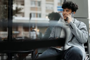 Camın önünde elinde kahve bardağıyla cep telefonuyla konuşan şık bir adam..