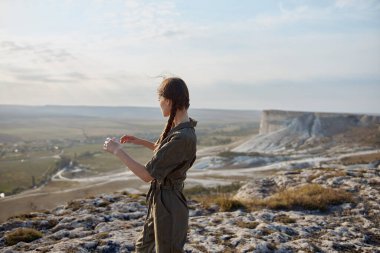 Dünyanın tepesinde bir kadın cep telefonuyla dağ gezisinde aşağıdaki vadiden nefes kesici manzaranın tadını çıkarıyor.