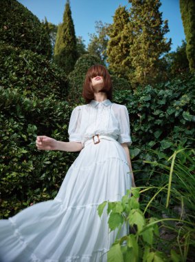 Beyaz elbiseli zarif bir kadın çiçek bahçesinin ortasında dikiliyor.