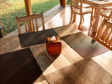 Sıcak ve davetkar bir yemek odası sahnesi, ahşap masa seti, peçete ve sandalye, rahat bir atmosfer yaratıyor..