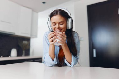 Mutfakta bir bardak süt içerken kulaklıkla müzik dinleyen bir kadın.
