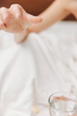 Yatakta bir bardak suyla yatan bir kadın, yatağa saçılmış haplar ve komodinin üzerinde bir hap şişesi..