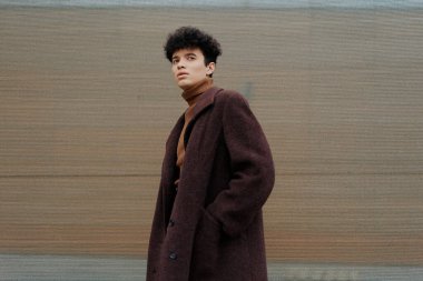 Moda adamı ve kahverengi paltolu kadın elleri ceplerinde bir sokakta dikiliyorlar..