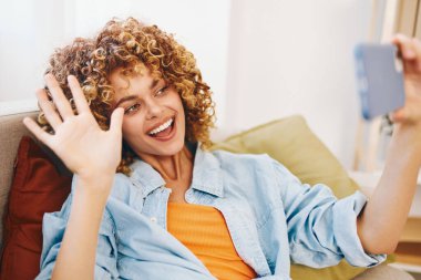 Konforlu Ev: Kanepede oturan, telefonu tutan, gülümseyen, çevrimiçi oyundan zevk alan, okuyan, selfie çeken, sohbet eden ve güzel bir oturma odasında arama yapan kadın