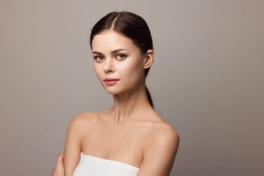 Gri bir arka planda çapraz kollarla poz veren güzel bir genç kadının portresi. Yakın çekim stüdyo çekimi onun kendine güvenini ve stilini yansıtıyor..