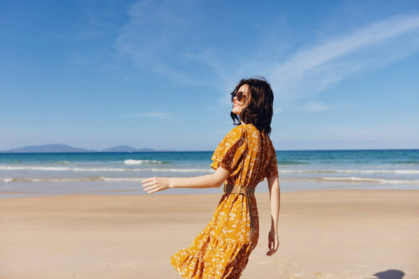 Happy woman enjoying the sunset on the beach with her hands up in a yellow dress