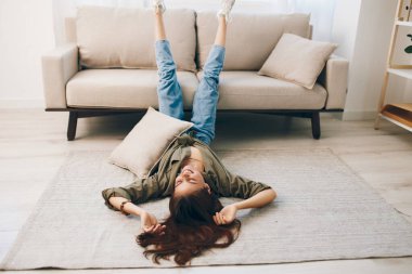 Sofa Serenity: Mutlu bir kadın rahatlatıcı, rahat bir şekilde uzanıyor, rahat bir modern dairede, tasasız bir yaşam tarzının tadını çıkarıyor