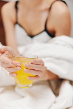 Bir bardak portakal suyuyla yatağa uzanmış beyaz çarşafla kaplanmış, başının altında yastıkla. Rahatlatıcı bir sabah sahnesi.