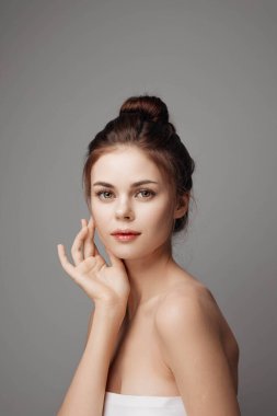 Kafasına havlu sarılmış, yüzü gri arka planda poz veren güzel bir genç kadın..