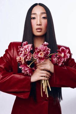 Beyaz arka planda uzun siyah saçlı ve kırmızı ceketli bir buket çiçek tutan kadın.